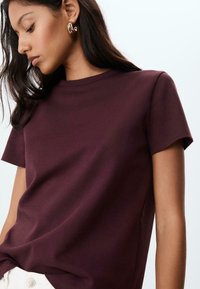 T-shirt bordeaux a maniche corte realizzato in morbido cotone, con un classico collo a giro e una texture liscia. Dettagli di cucitura discreti alle cuciture.