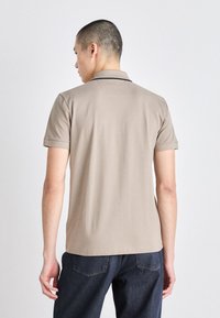 Beige polo tričko s krátkým rukávem, hladkou texturou a límcem. Obsahuje jemné švy na ramenou a zádech.