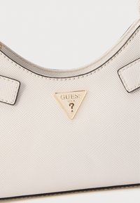 Borsa bianca con texture e forma curva, caratterizzata da un logo triangolare dorato e rifiniture nere. Due piccoli dettagli quadrati sulla maniglia.