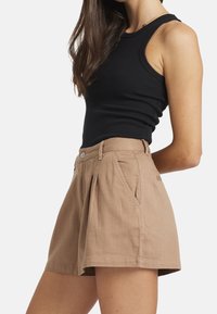 Vaaleanbeige shorts, joissa on muotolaskokset edessä, sivutaskut ja istuva vyötärö. Valmistettu teksturoidusta kankaasta.