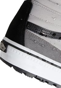 Gros plan sur une sneaker Vans noire, grise et blanche avec des gouttelettes d'eau mettant en valeur son matériau résistant à l'eau.