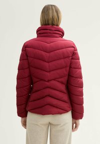 Rode pufferjack met chevrondetails, hoge kraag en zijzakken. Heeft een getailleerde pasvorm, gestructureerd oppervlak en een gladde stof.