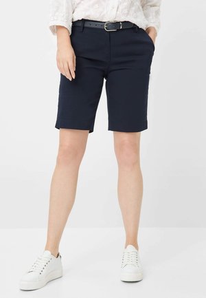 Dunkelblaue Baumwollshorts mit glatter Textur, Gürtelschlaufen und geradem Schnitt, kombiniert mit weißen Sneakers mit flachem Profil und Schnürsenkeln.