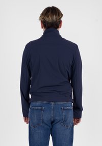 Giacca leggera blu navy con colletto alto e maniche lunghe, realizzata in tessuto morbido. Abbinata a jeans di denim. Vista posteriore.