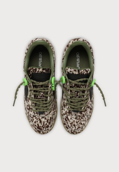 Paire de baskets écrues avec un motif tacheté marron, des lacets vert olive et des bloque-lacets vert néon, vues de dessus sur un fond clair.