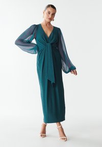 Türkises langes Kleid mit fließenden, durchsichtigen Ärmeln, einem V-Ausschnitt und gerafftem Taillendetail. Glatte Textur mit einer Bindefunktion an der Vorderseite.