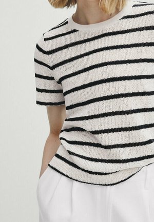 Person wearing a short-sleeve knitted white sweater with black horizontal stripes and white pants, standing against a neutral background.