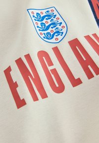 Tissu crème avec le blason de l'équipe de football d'Angleterre affichant trois lions bleus et un texte rouge indiquant "ENGLAND."