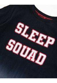 Czarny bawełniany t-shirt z wyraźnym białym napisem "SLEEP SQUAD" obrysowanym na czerwono, okrągły dekolt i standardowe krótkie rękawy.