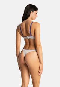 Ensemble de lingerie blanche avec accents bleus ; comprend un soutien-gorge à bretelles ajustables et un string assorti. Présente une texture lisse et un design minimaliste.