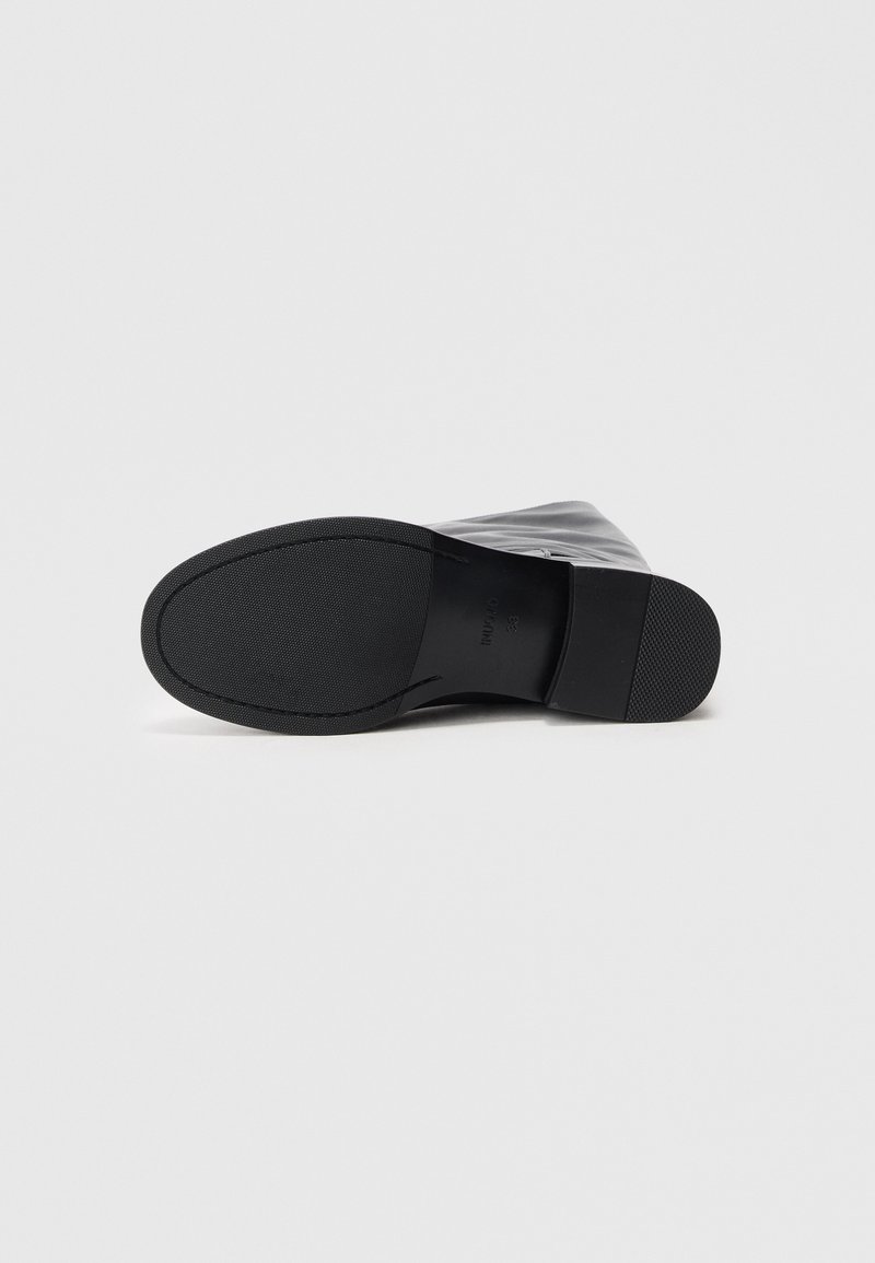 Schwarzer Stiefel mit einer glatten, glänzenden synthetischen Oberseite, runder Zehenpartie und einer flachen Gummisohle. Verfügt über subtile Nähte und keine sichtbaren Beschläge.