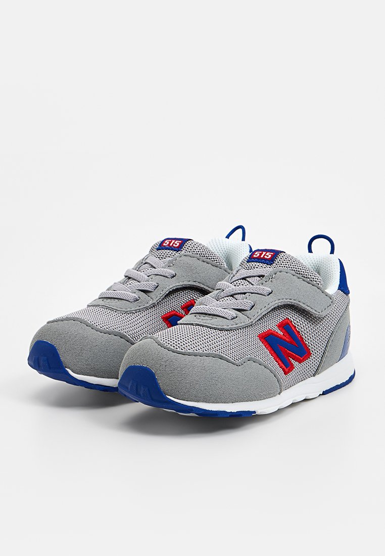 Zapatillas de malla y ante en gris con acentos azules, que presentan un logo rojo, cordones y una suela blanca. Diseñadas para ofrecer comodidad y soporte.