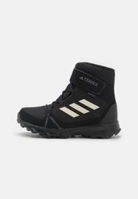 Botas de senderismo altas negras con parte superior de malla y sintético, suela de goma, correa de Velcro y tres rayas diagonales blancas en el costado.