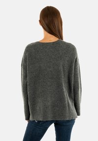 Donkergrijs oversized sweater met een zachte textuur, brede mouwen, geribbelde zoom en een losse pasvorm, gecombineerd met donkerblauwe jeans.