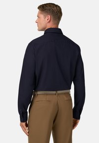 Námořnická košile s límečkem, dlouhými rukávy a hladkým povrchem; v kombinaci s béžovými kalhotami a pleteným páskem.