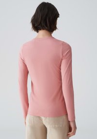 Langärmliges Shirt aus weichem rosa Stoff mit runden Halsausschnitt und glatter Textur, das eine taillierte Passform und dezente Nähte an den Schultern aufweist.