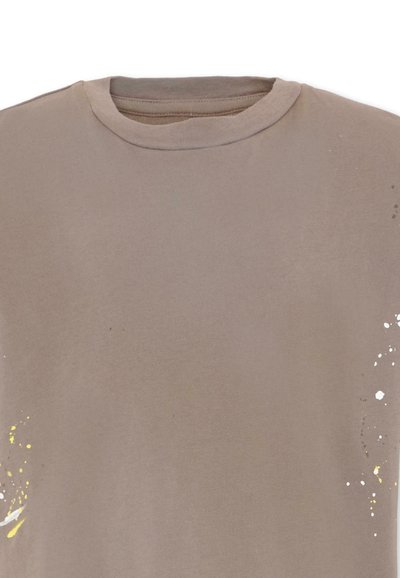 Maglietta beige con scollo rotondo e sottili schizzi di vernice gialla e bianca sui lati inferiori sinistro e destro.