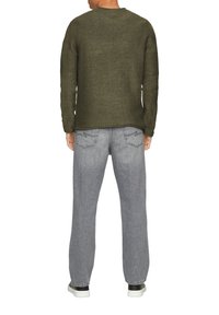 Oliwkowy sweter z dzianiny z okrągłym dekoltem, zestawiony z jasnoszarymi spodniami o szerokich nogawkach. Sweter ma widoczne szwy i luźny krój.
