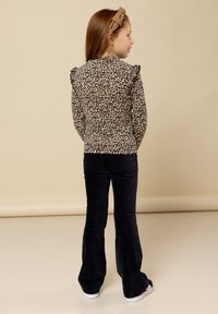 Langarmige top met luipaardprint en ruches op de schouders, gecombineerd met donker flanellen wijde broek. Haarband voegt een bijpassend accent toe.