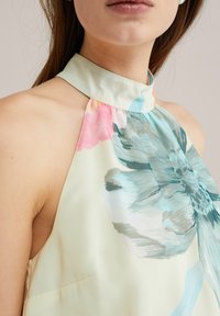 Top halter cu imprimeu floral în galben deschis, cu accente de albastru, roz și verde. Textură mătăsoasă, cu guler structurat și design plisat.