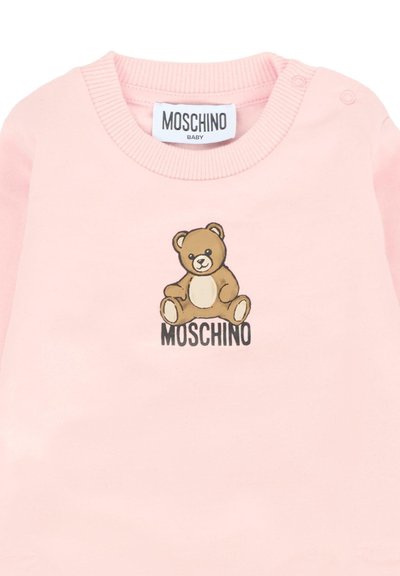 Jasnoróżowy bodziak dla niemowląt z grafiką misia oraz napisem "MOSCHINO" na piersi, z napami na ramieniu.
