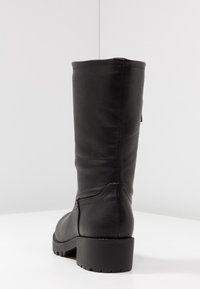 Bota alta de cuero negro con un acabado texturizado, suela resistente y un tacón modesto. Presenta una costura lateral para una continuidad en el diseño.