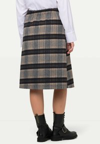 Wollen geruite rok met grijs, zwart en bruin gestreept patroon; enkel-lang met een elastische tailleband; gecombineerd met zwarte legerboots.