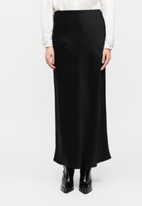 Μαύρη σατέν φούστα μάξι με λεία υφή και ίσια σιλουέτα. Συνδυάζεται με λευκό πουκάμισο με διακοσμημένες μανσέτες.