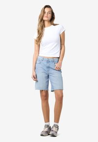 Pantaloni corti in denim azzurro chiaro con bordi sfilacciati, abbinati a una t-shirt bianca aderente e scarpe da ginnastica grigie. Design semplice e casual.