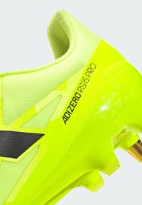 Světlé žluté fotbalové kopačky s texturovaným svrchním materiálem, černými akcenty a elegantním designem. Obsahují zlaté kolíky a branding "ADIZERO RS15 PRO".