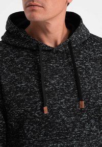 Dunkelgrauer Hoodie mit strukturiertem, meliertem Muster. Verfügt über eine Kängurutasche, schwarze Kordeln und tanfarbene Lederakzente am Hals.