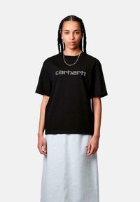 Camiseta de algodón negra de mangas cortas con un logo gris de "Carhartt" en el pecho. Combinada con una falda de mezclilla gris clara.
