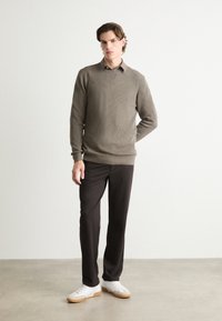 Suéter de punto acanalado marrón claro, pantalones oscuros y zapatillas blancas. El suéter cuenta con un cuello redondo y puños ajustados. Diseño sencillo, sin patrones.