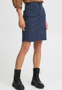 Mörkblå denimpennkjol med medelhög midja, fem-knappslås framtill och två sidofickor. Kombinerad med svarta snörboots.