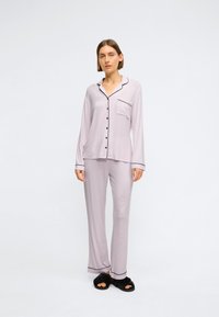 Set de pijama de culoare mov deschis cu piping negru. Bluză cu mânecă lungă, cu nasturi și buzunar; pantaloni asortați. Textura materialului este moale și netedă.