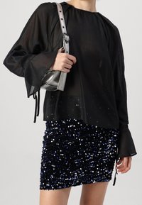 Svart genomskinlig blus med lösa ärmar, i kombination med en glittrig minikjol i svart och blå paljetter. Axelväska i metalliskt silver.