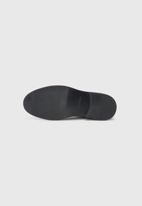 Suela de zapato negra con una textura suave, punta ligeramente redondeada y forma contorneada. Mínima marca visible en la superficie superior.