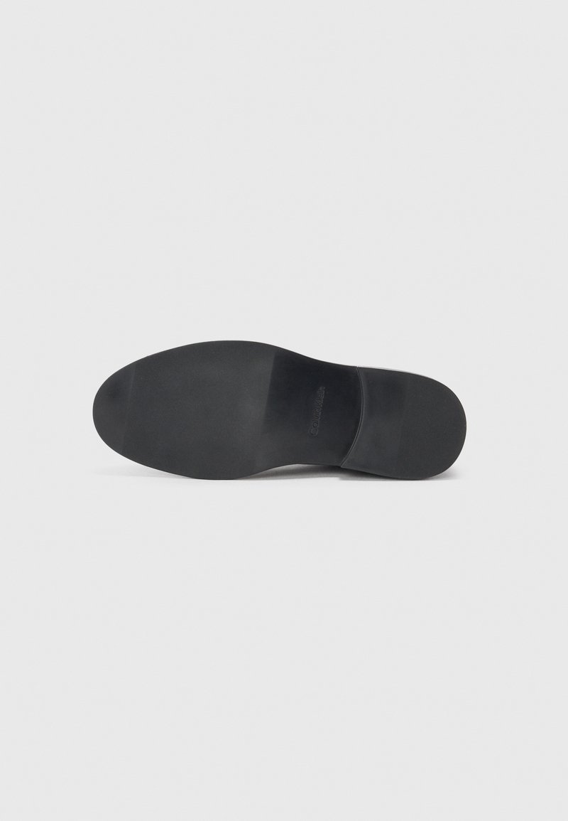 Semelle de chaussure noire avec une texture lisse, pointe légèrement arrondie et forme profilée. Marquage minimal visible sur la surface supérieure.