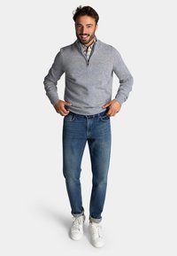 Lichtgrijze quarter-zip trui met geribbelde manchetten, blauwe geruite shirt eronder, gecombineerd met donkerblauwe jeans en witte sneakers.