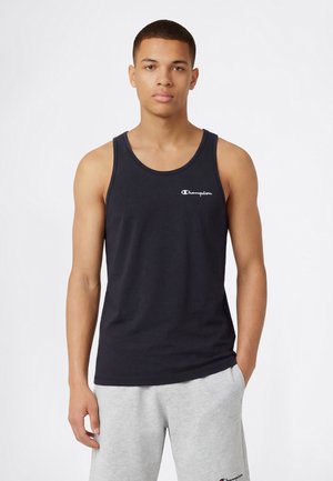 Canotta in cotone blu navy con scollo rotondo e bordi cuciti. Presenta un logo "Champion" bianco sul petto. Il modello la indossa con pantaloni della tuta grigi.