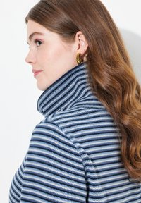 Maglione a righe in blu navy e azzurro chiaro con colletto alto. Texture liscia e tessuto morbido. Orecchino ad anello dorato come accessorio.