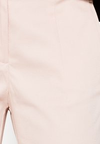 Pantalon rose clair en tissu texturé avec une finition lisse. Caractéristiques d'un devant plat et de détails de couture sur les côtés.