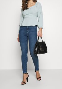 Top peplum blu chiaro con maniche arricciate e dettagli con bottoni, abbinato a jeans skinny blu scuro. Borsa nera con motivo coccodrillo, tacchi a strappo.