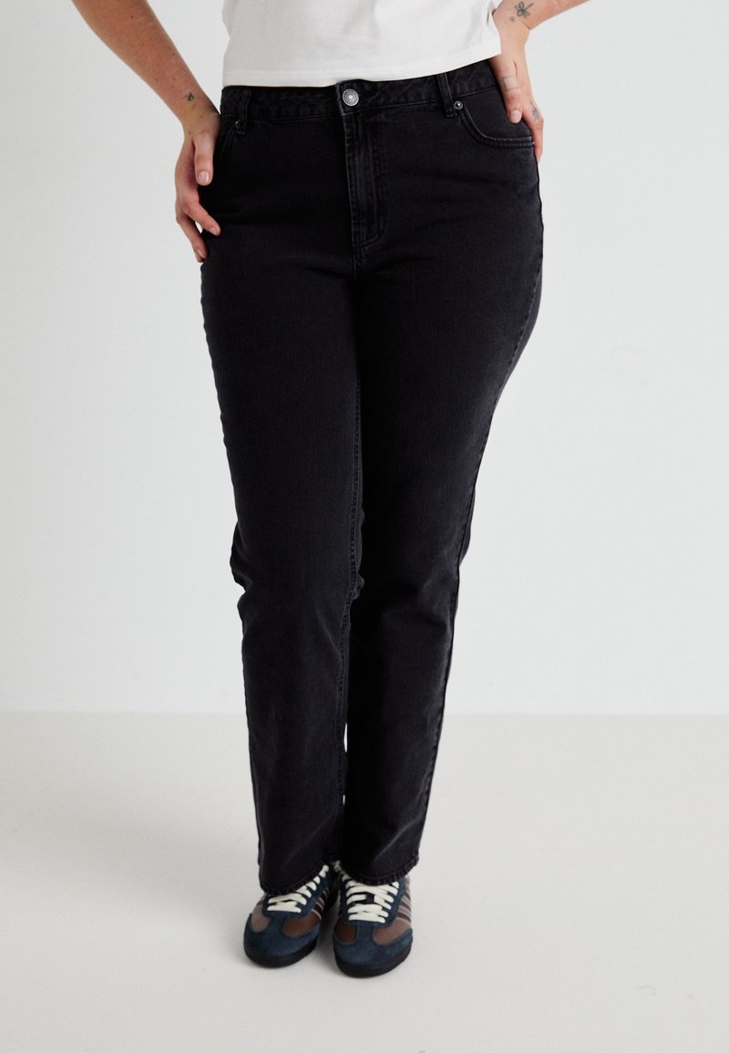 Black denim jeans with a straight-leg fit, featuring front pockets, a button closure, and subtle stitching details. Paired with multicolored sneakers.