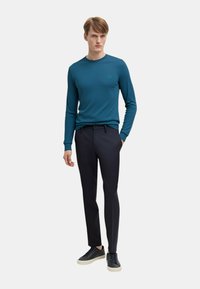 Maglietta a maniche lunghe color turchese con scollatura rotonda, abbinata a pantaloni scuri e sneakers nere. Design semplice con dettagli minimi.