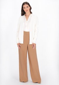 Weißer Cardigan mit strukturierter Oberfläche, kombiniert mit einer hellen Bluse und beigen, weit geschnittenen Hosen, was eine neutrale Farbpalette ergibt.