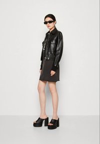 Czarna skórzana kurtka z dużymi klapami, zestawiona z ciemnoszarym mini dresskiem i masywnymi czarnymi platformami z odkrytymi palcami.
