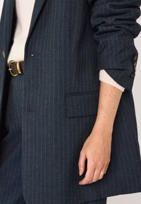 Blazer a righe blu navy realizzato in tessuto texturizzato con una tasca sul petto, dotato di bottoni color oro sui polsini e una vestibilità morbida.