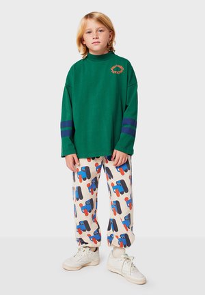 Sweatshirt oversized en coton vert avec des accents rayés bleus, associé à un pantalon crème avec un motif graphique ludique et des baskets blanches.