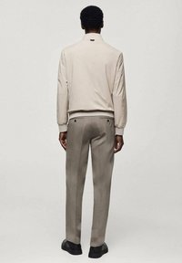 Hellbeige Bomberjacke mit Stehkragen, kombiniert mit hellgrauen Hosen; verfügt über dezente Nähte und minimalistische Designdetails.